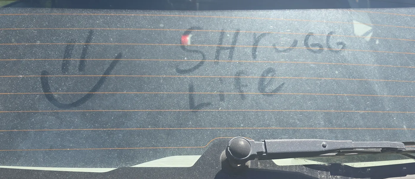 SHRUGG Life and a smiley drawn in dust on a car window